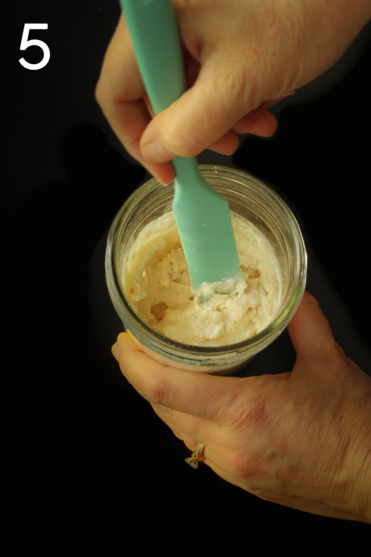 stirring together sourdough starter in mason jar on black table.