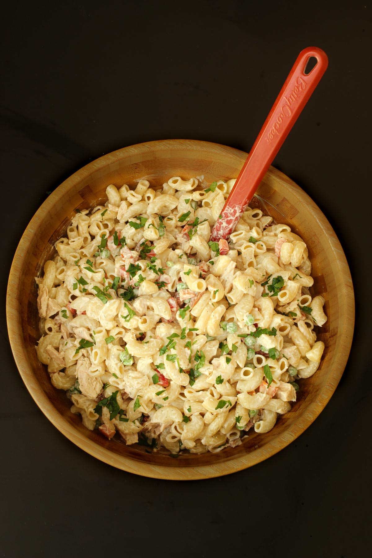 the tuna mac salad completely assembled in the wooden bowl with a red spoon