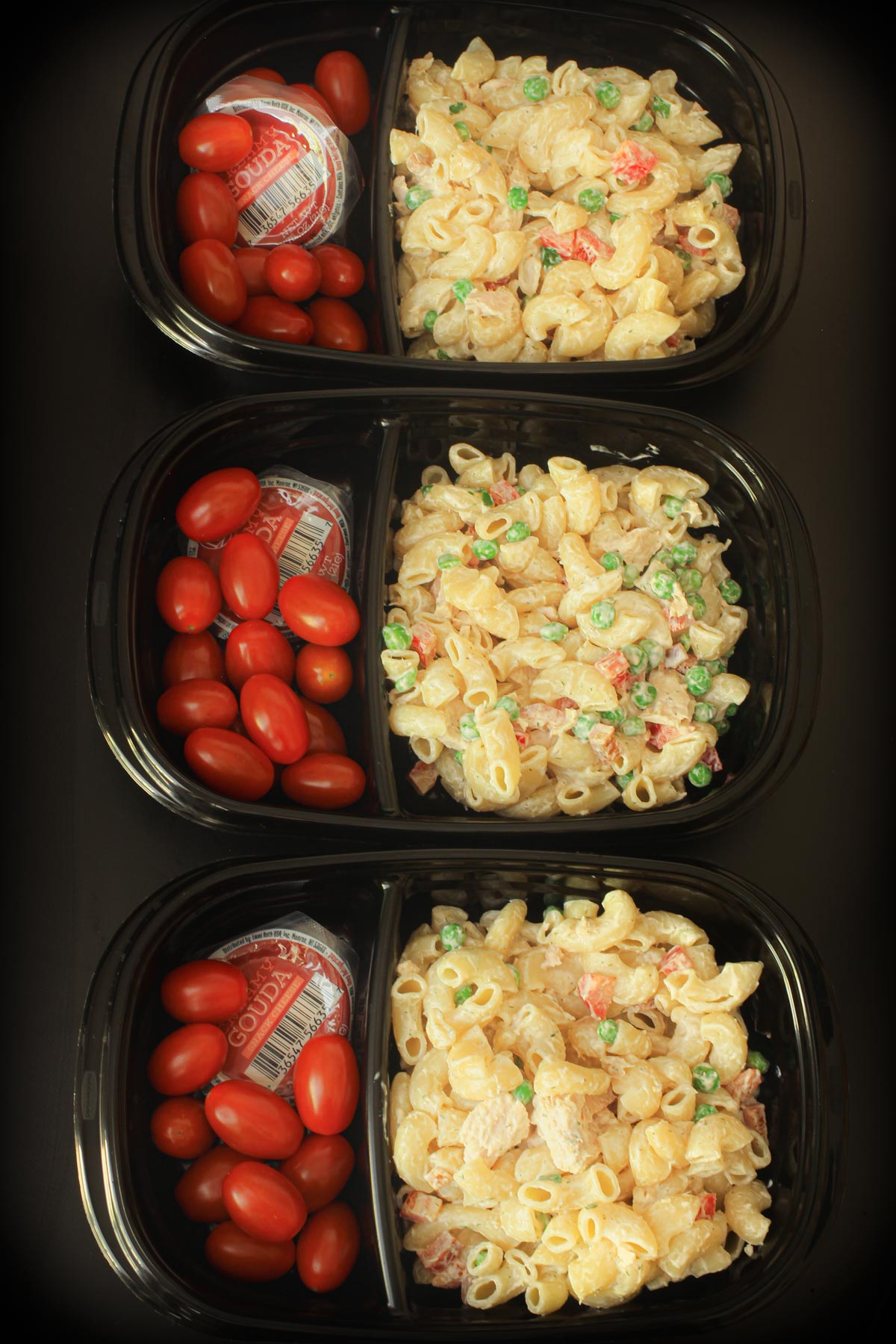 three black meal prep boxes packed with tuna mac salad, grape tomatoes, and snacking cheese.