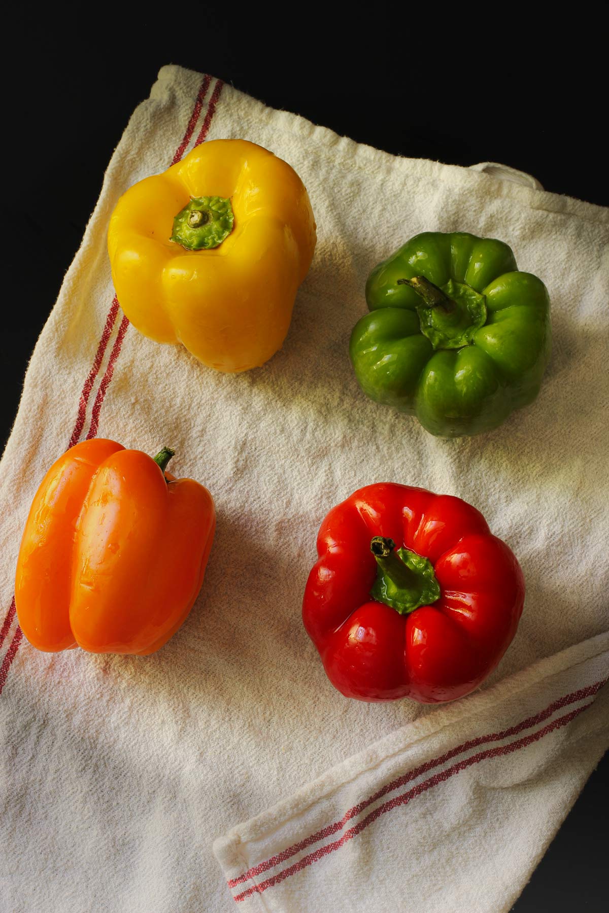 orange, yellow, green, and red bell peppers on a white tea towel.