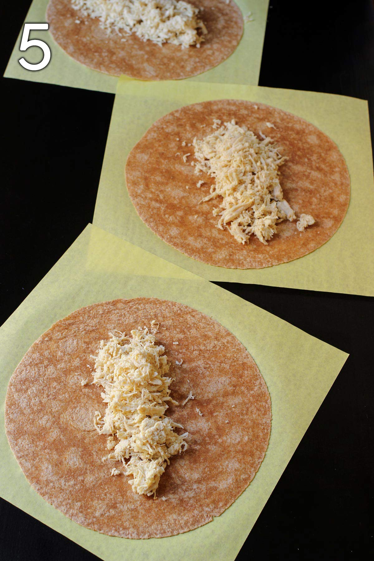 chicken distributed on whole wheat tortillas in assembly line.