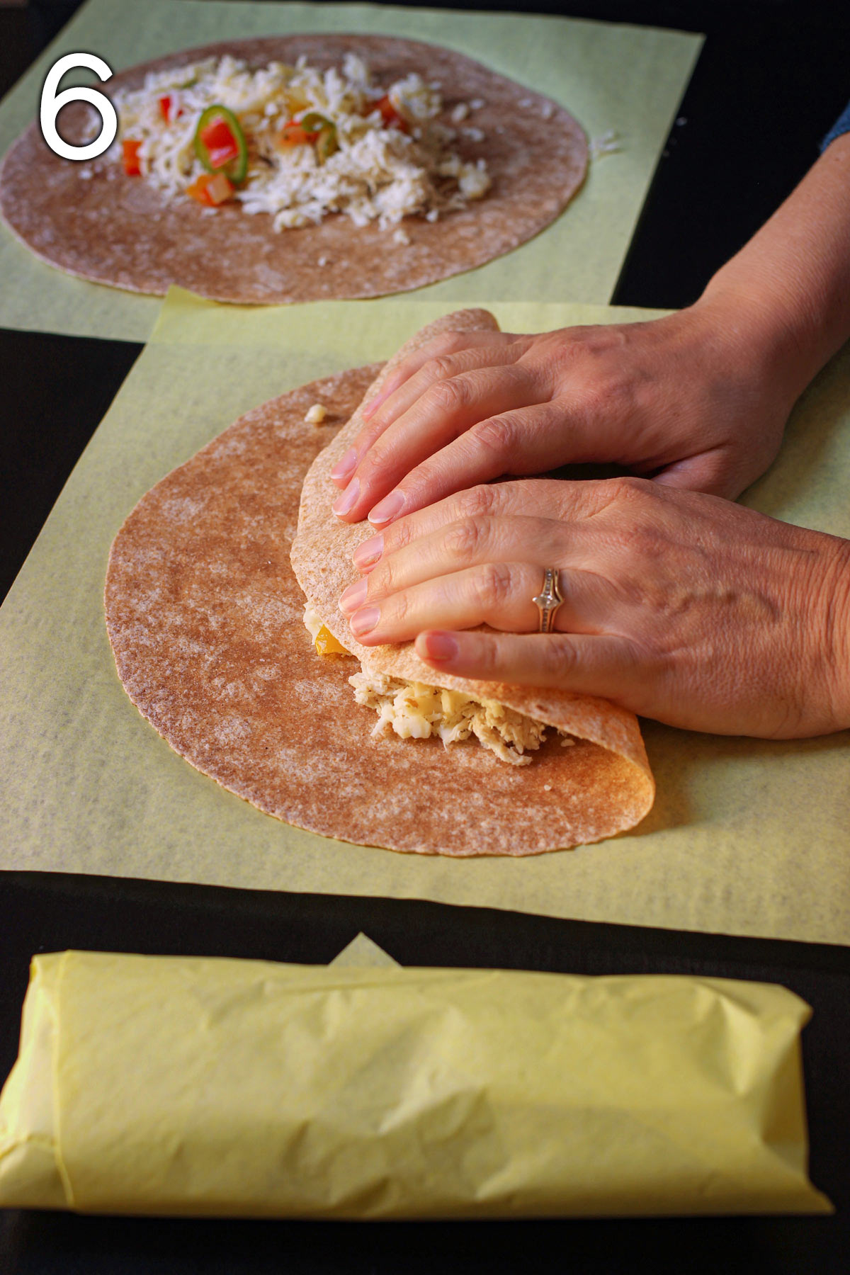 hand folding the bottom of the whole wheat tortilla over the filling of the burrito.
