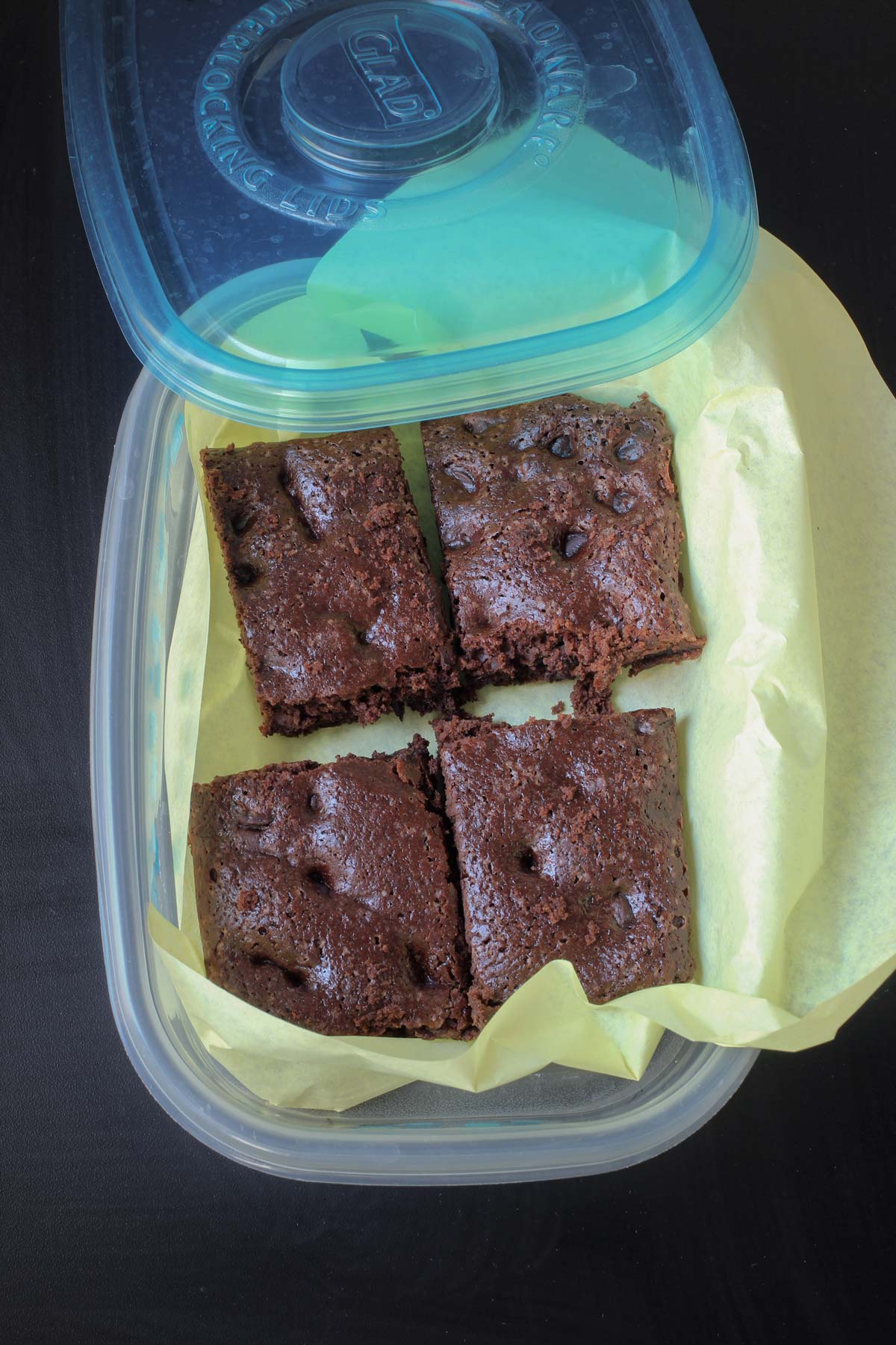 brownies sliced and arranged in a plastic container with a lid lined with deli wrap.