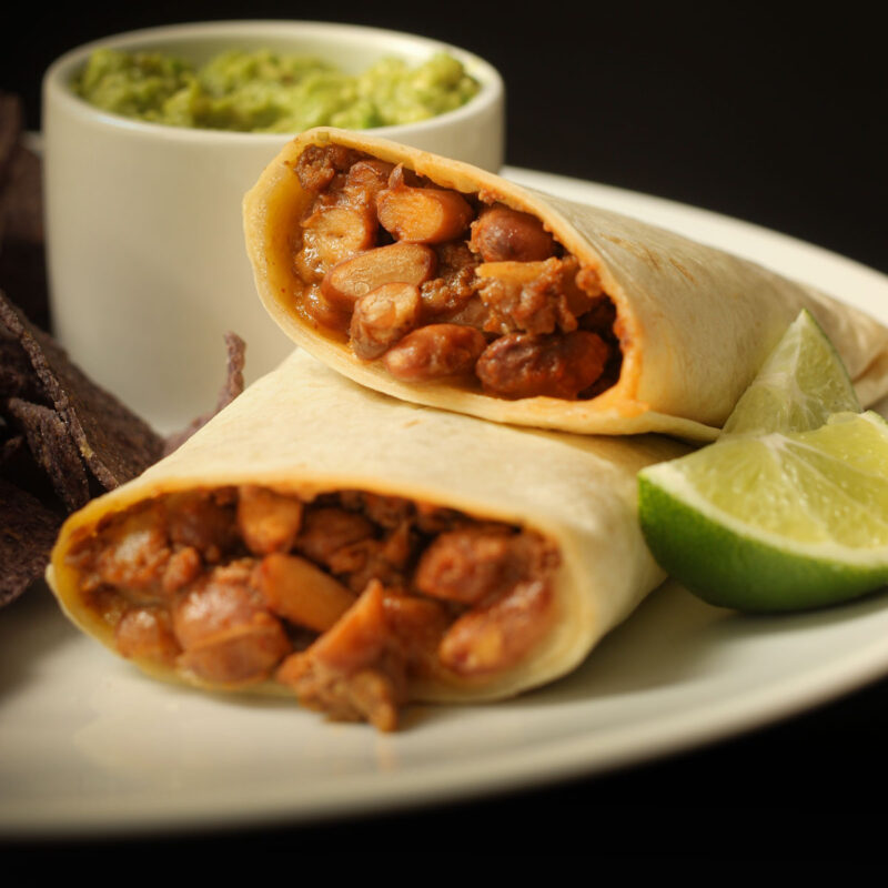 halves of chili cheese burrito stacked on a plate with chips and guacamole.