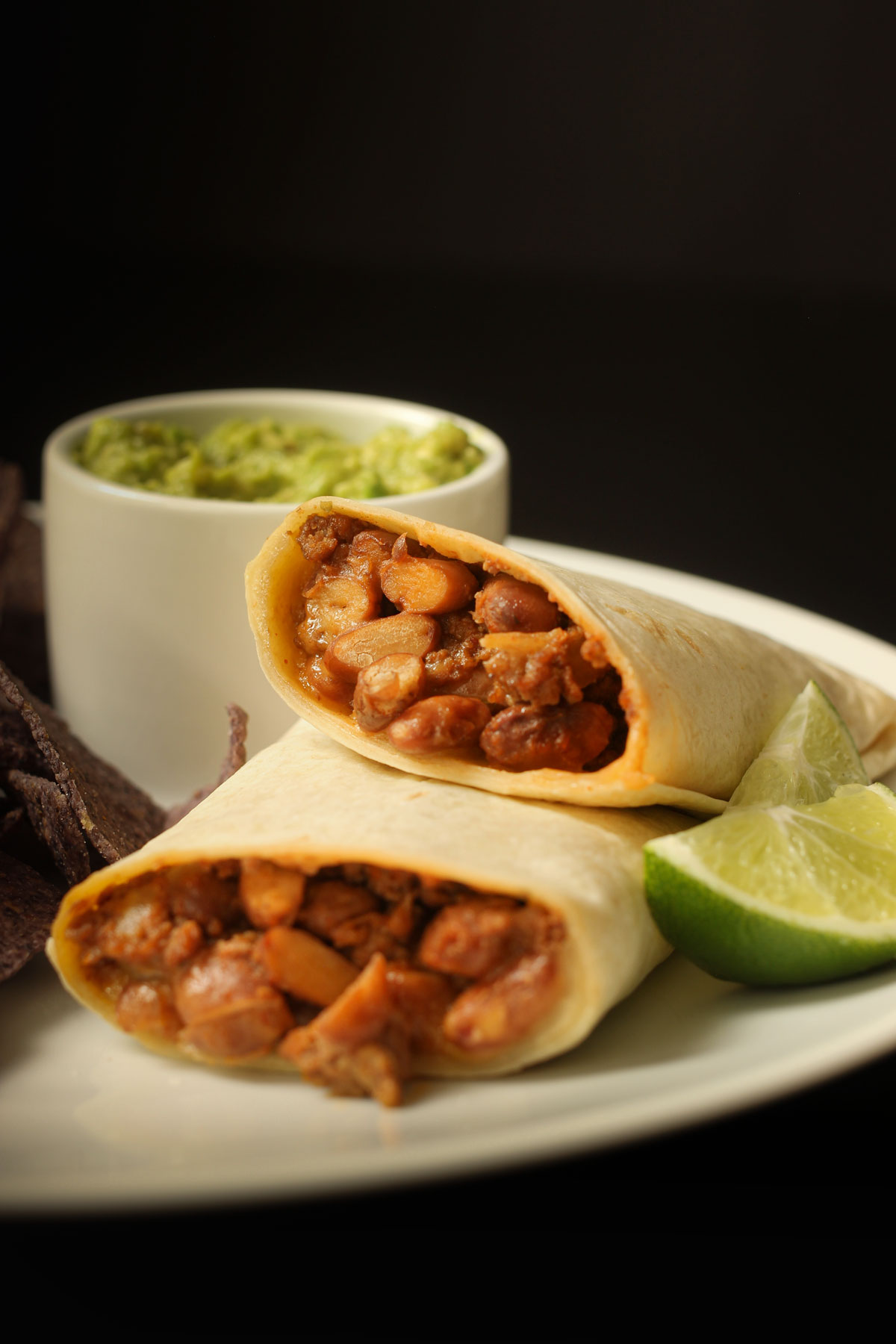 chili cheese burrito cut in half on white plate with lime wedge and guacamole cup.