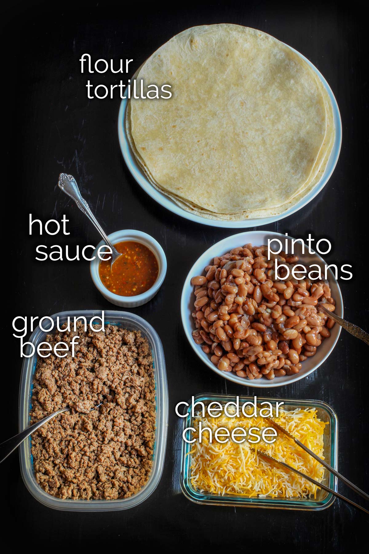 ingredients for beef chimichangas laid out on black table top.