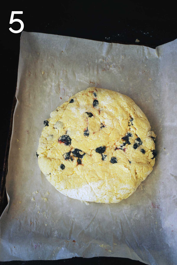 scone dough shaped into a thick round on the parchment paper-lined baking sheet.