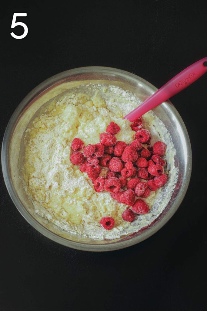 adding wet ingredients to dry and then frozen raspberries in large metal mixing bowl.