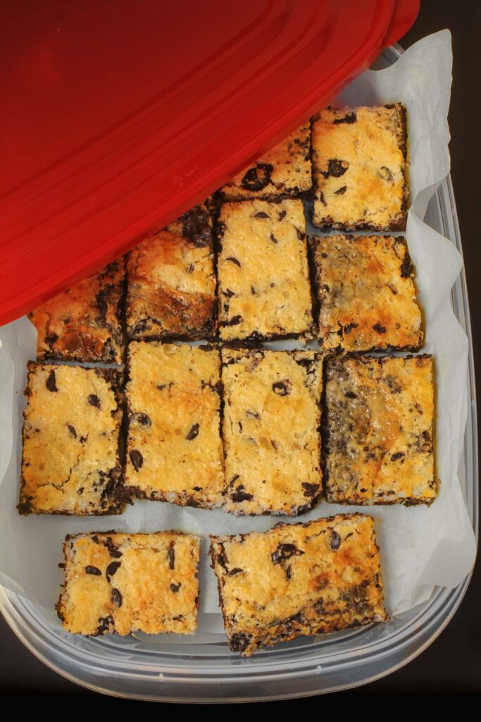 magic bars cut into pieces in a plastic container with a red lid.
