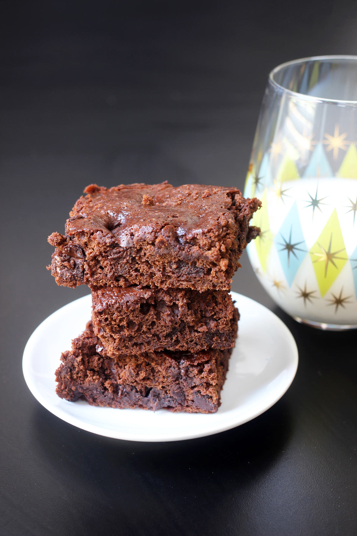 brownies stacked on small white plate next to glass of milk.