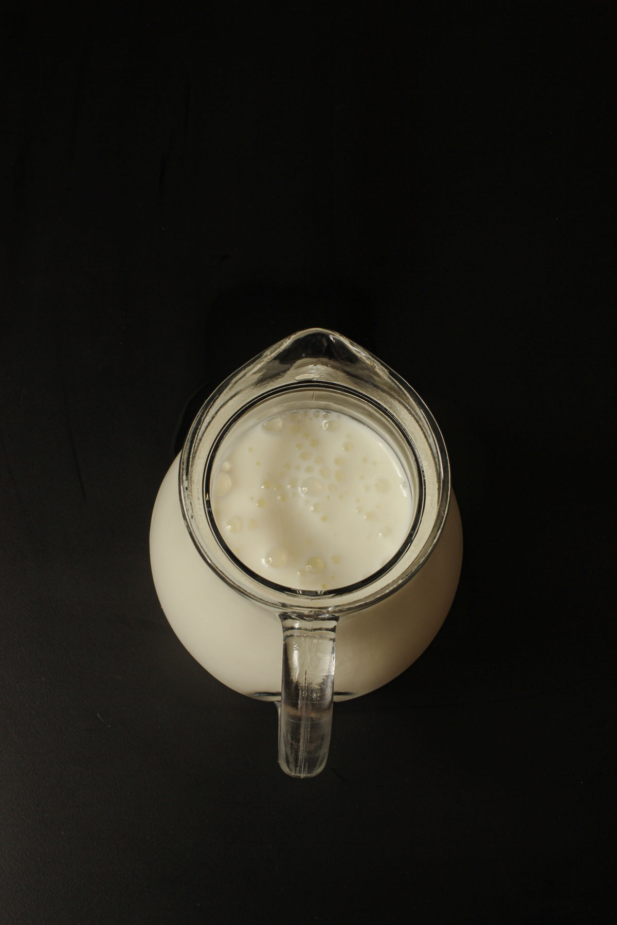 overhead view of a small glass pitcher filled with bubbly buttermilk on a black background.