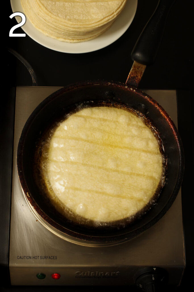 skillet on medium heat with hot oil and corn tortilla frying.