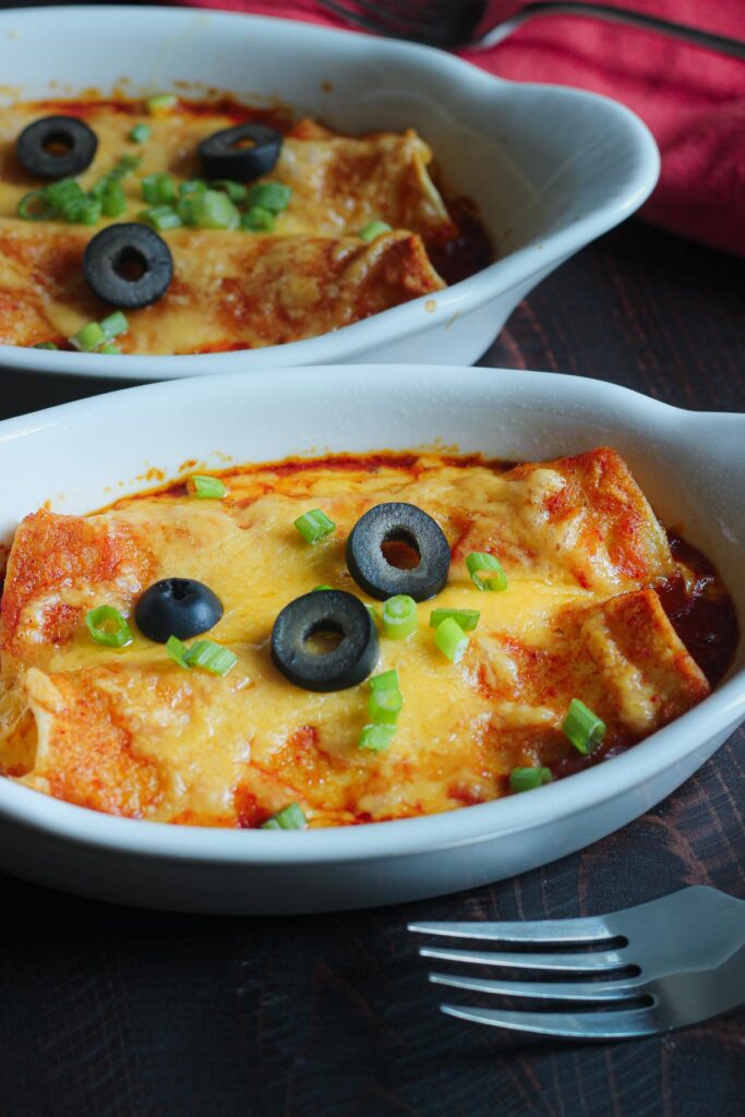 gratin dishes each holding two cheese enchiladas topped with sliced olives and green onions.