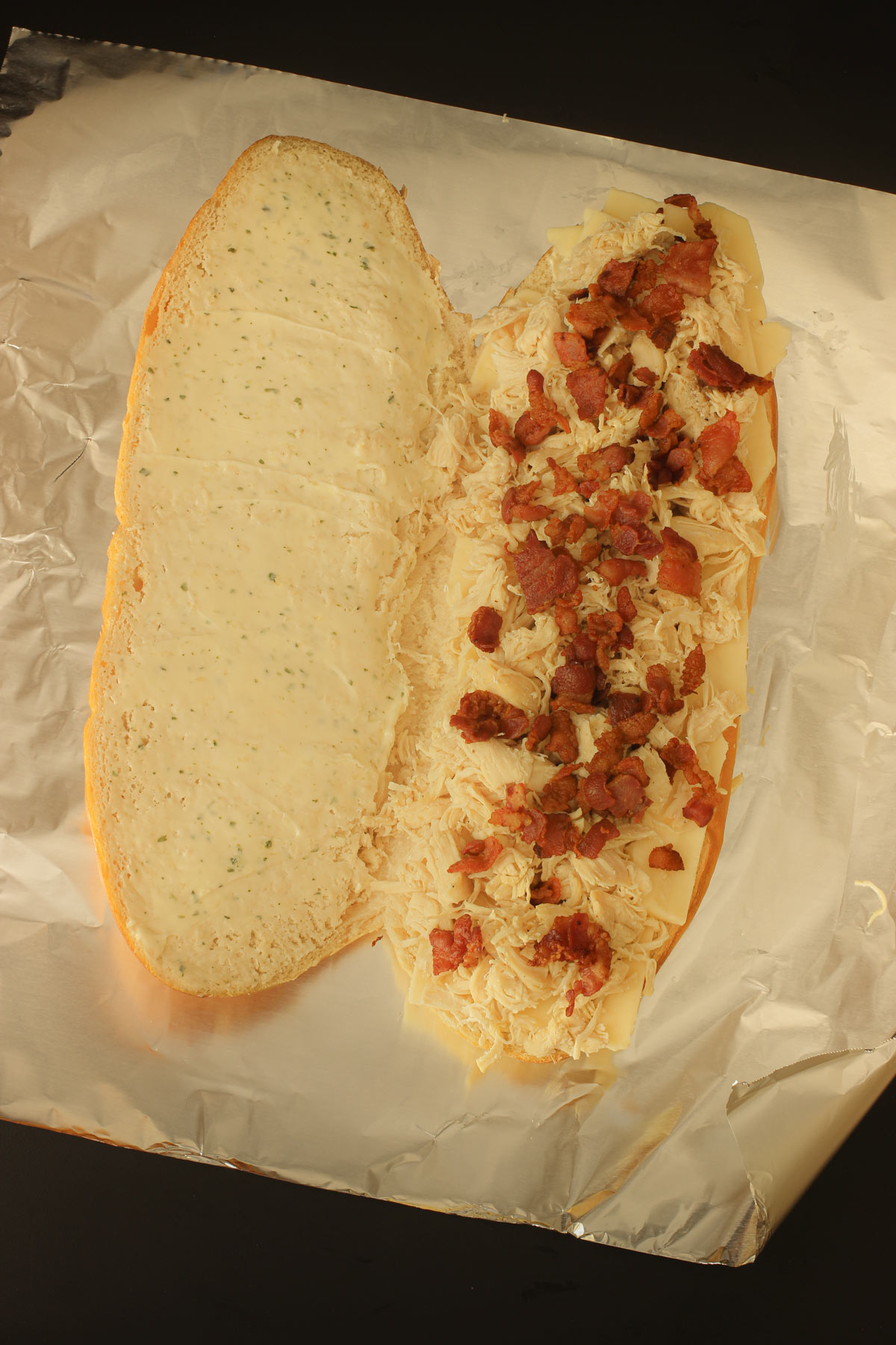 bacon crumbles atop the chicken on one side of the French loaf on foil.