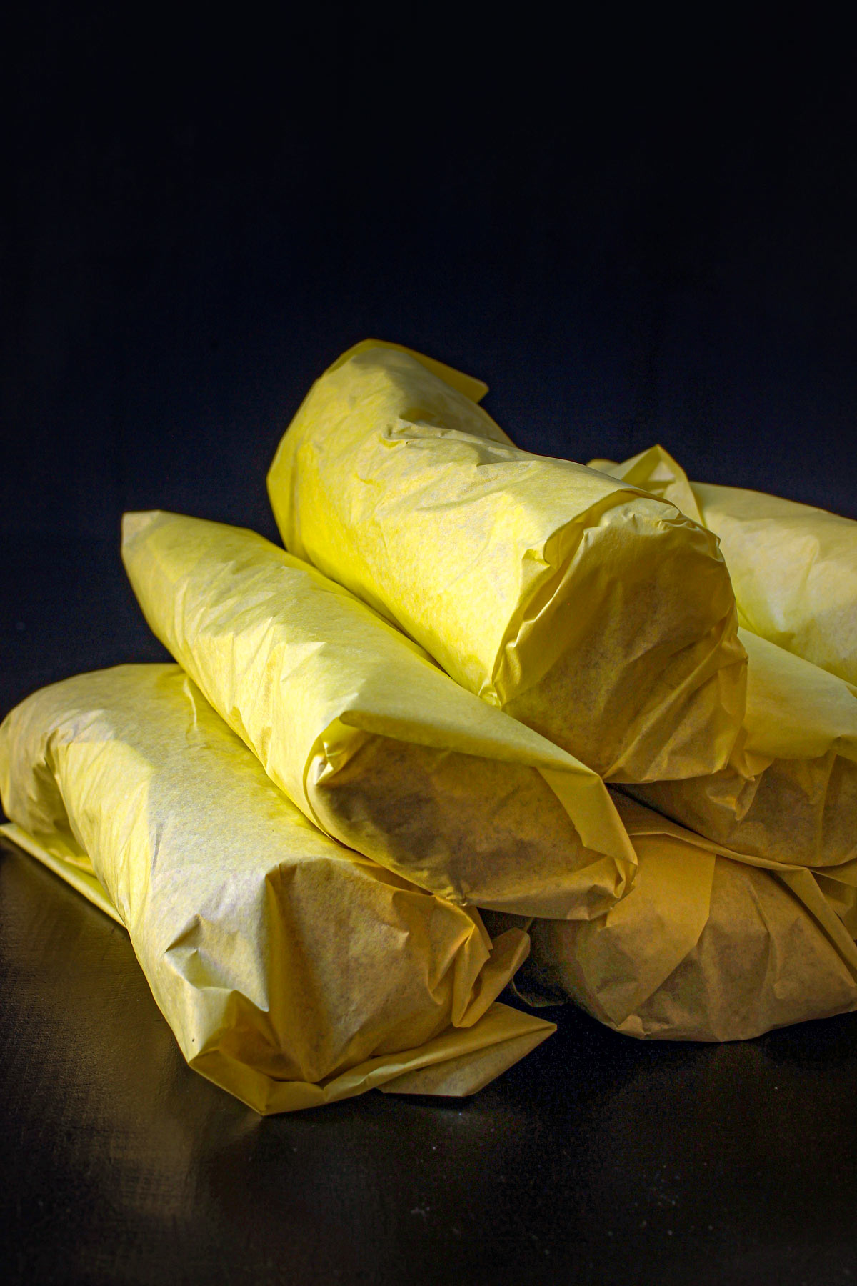 stack of rolled and wrapped fajita burritos on black tabletop.