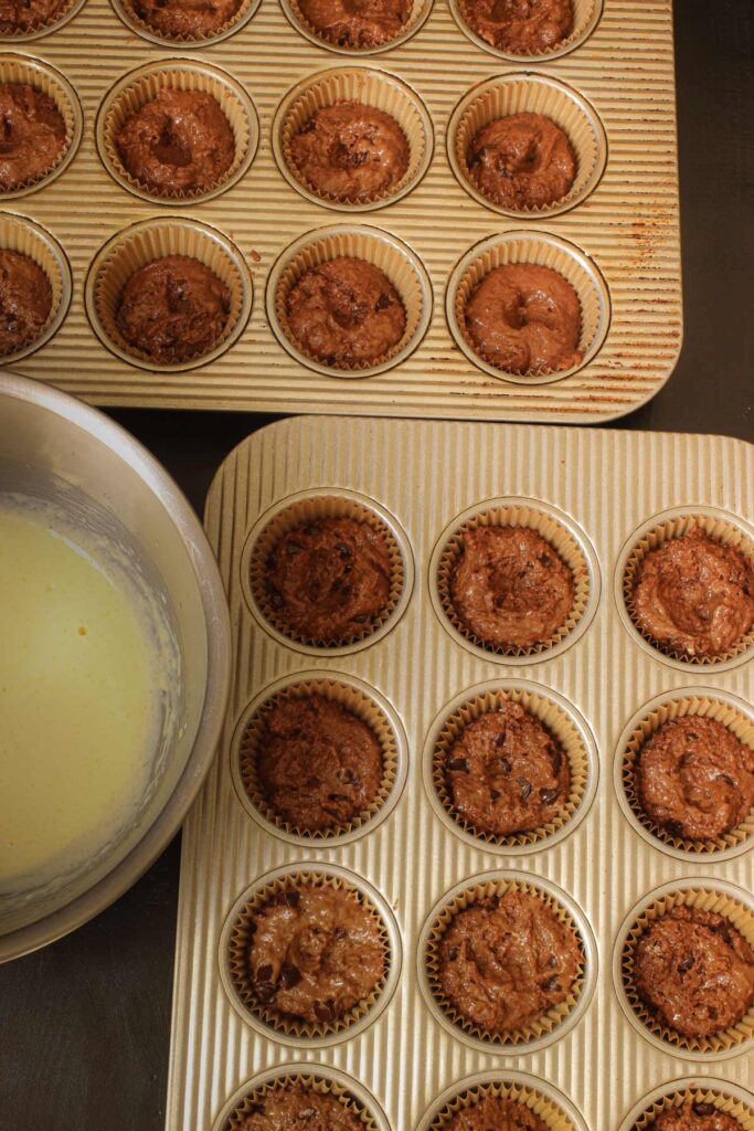 muffin pans lined with chocolate batter next to bowl of cream cheese topping.