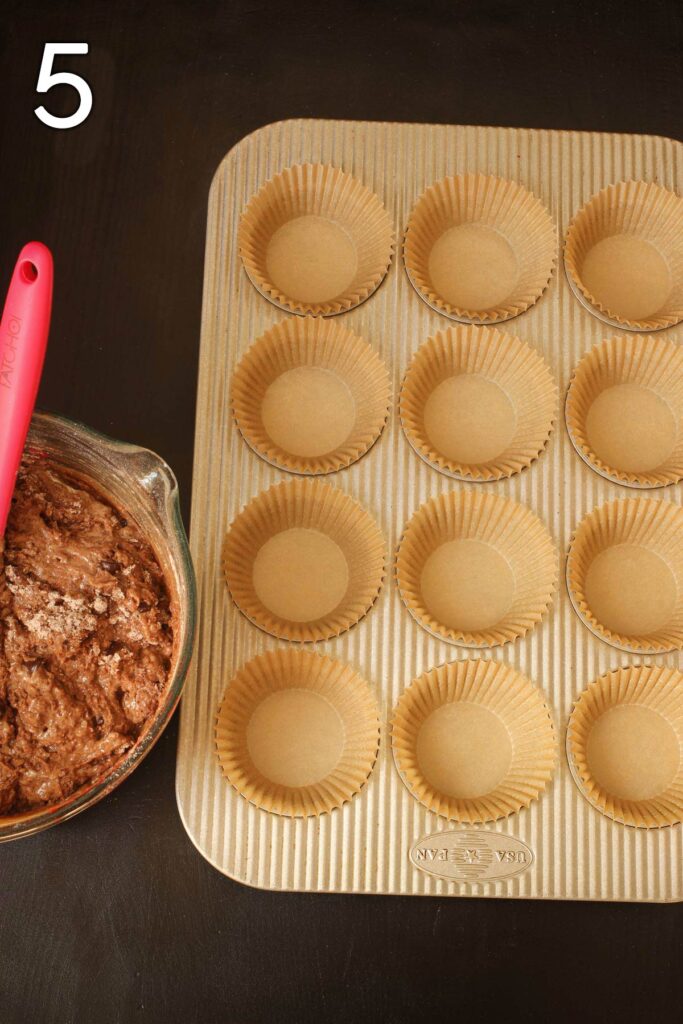 muffin pan lined with papers next to bowl of batter.