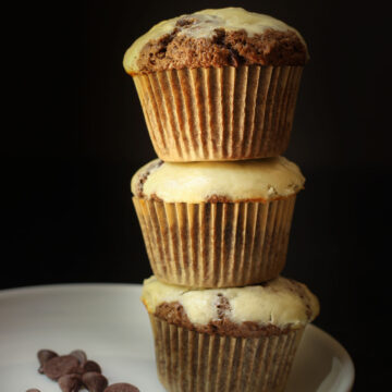 three chocolate cream cheese muffins stacked on a plate with chocolate chips.