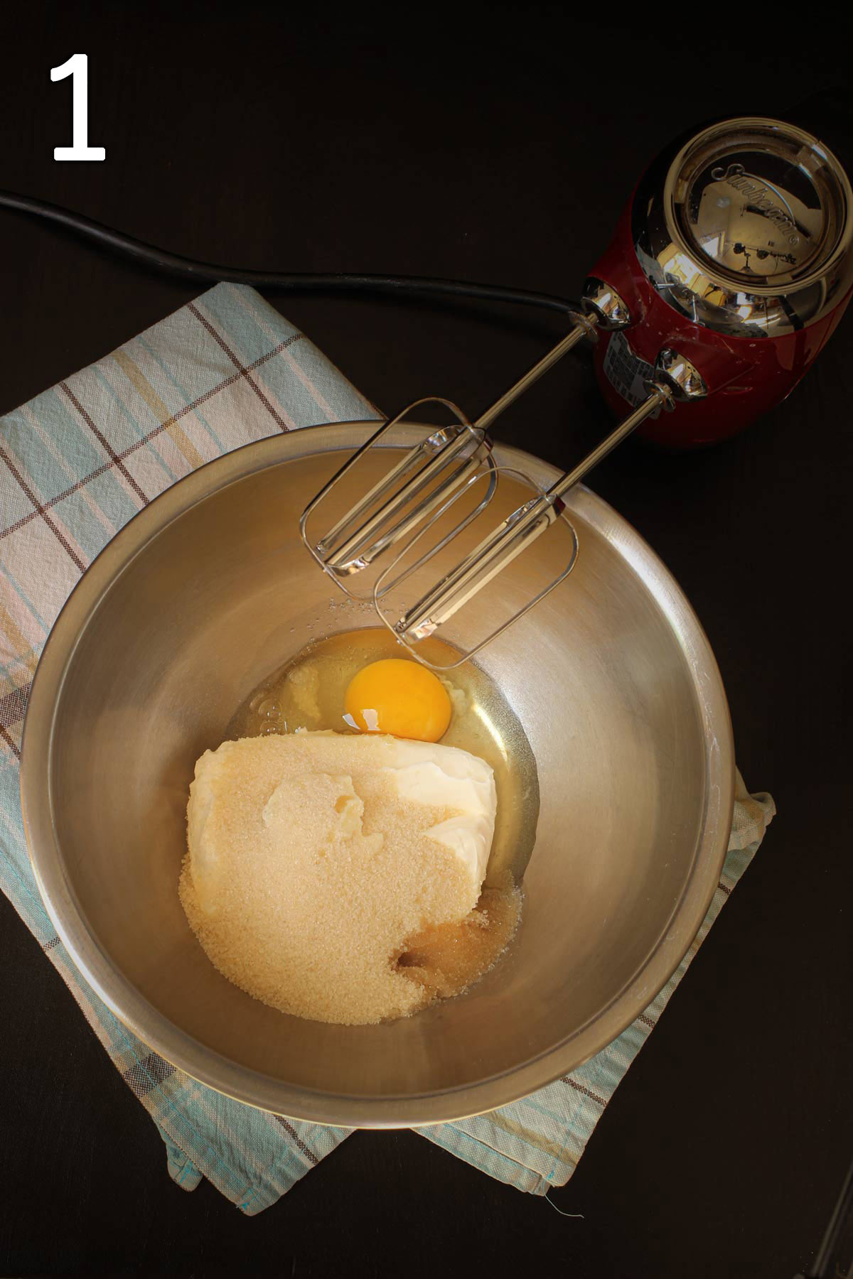 cream cheese, egg, sugar, and vanilla in a mixing bowl next to hand mixer.