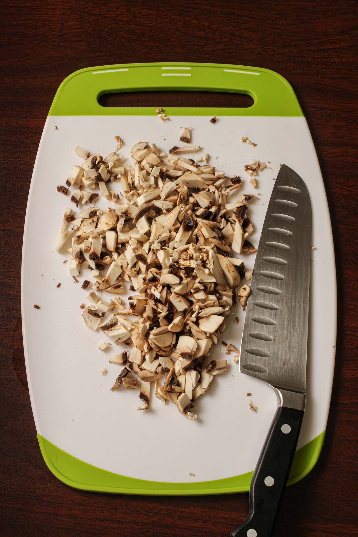 chopped mushrooms and knife on white and green cutting board.