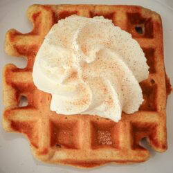 overhead shot of cinnamon waffle topped with whipped cream and cinnamon sugar.
