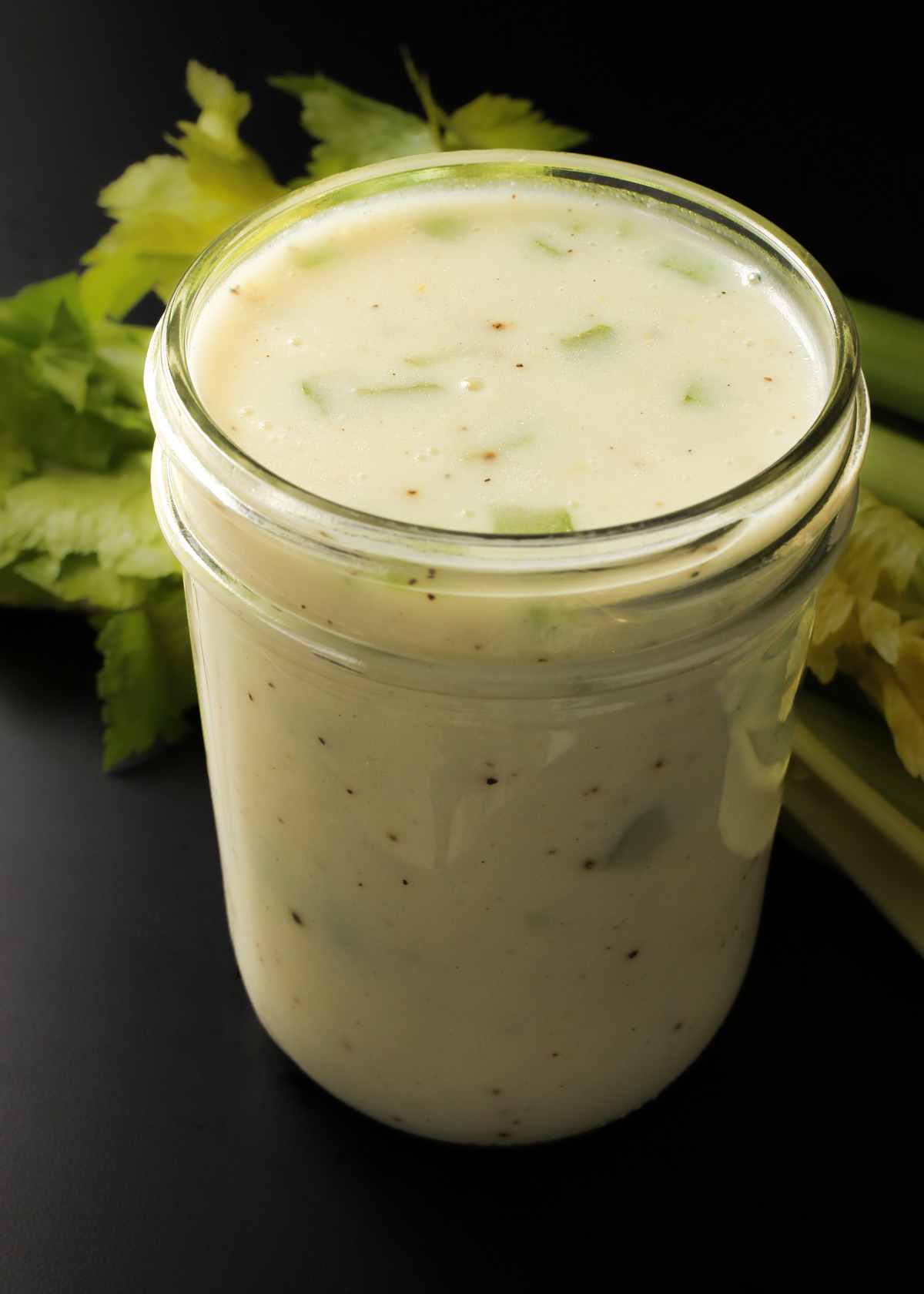 jar of homemade cream of celery soup on black table with stalk of celery in background.