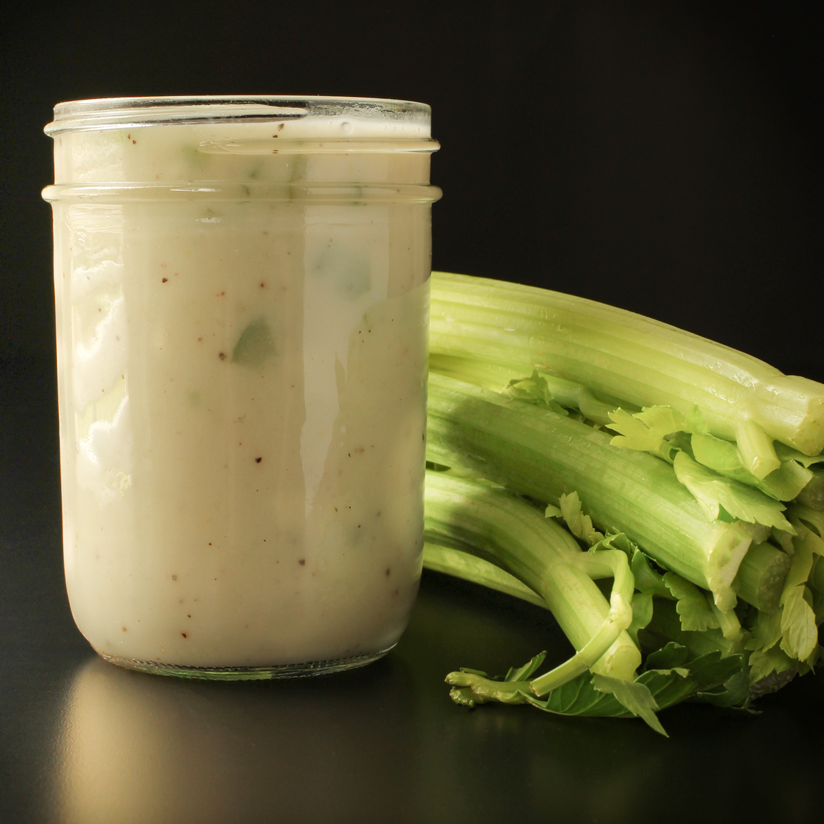 jar of cream of celery soup on black table with ribs of celery nearby.
