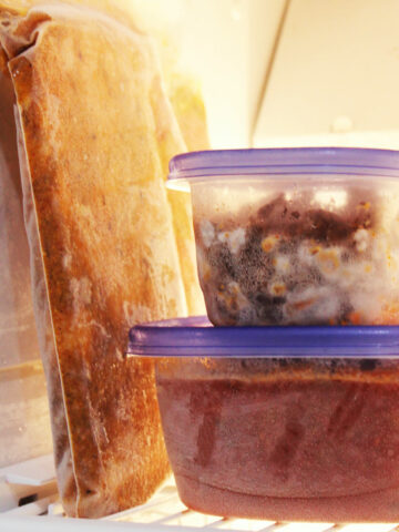 freezer meals in bag and plastic containers stacked on freezer shelf.