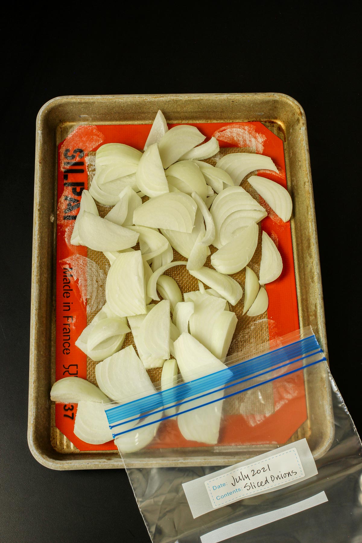 frozen sliced onions on quarter sheet pan with labeled ziptop freezer bag.