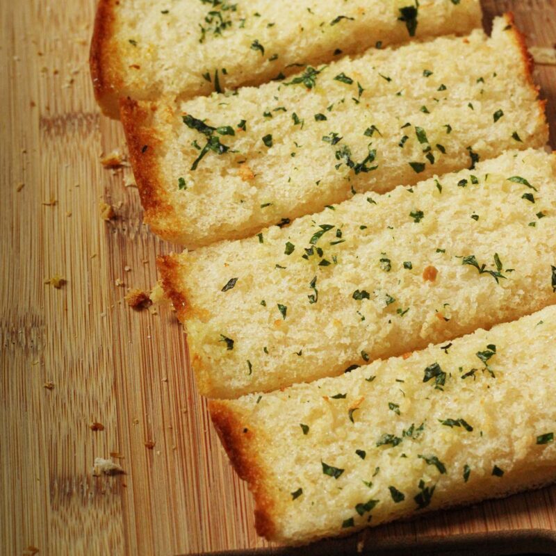 loaf of toasted frozen garlic bread, cut into slices on cutting board with scattered crumbs.
