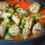 close up of gluten-free meatballs in pot of sauce.