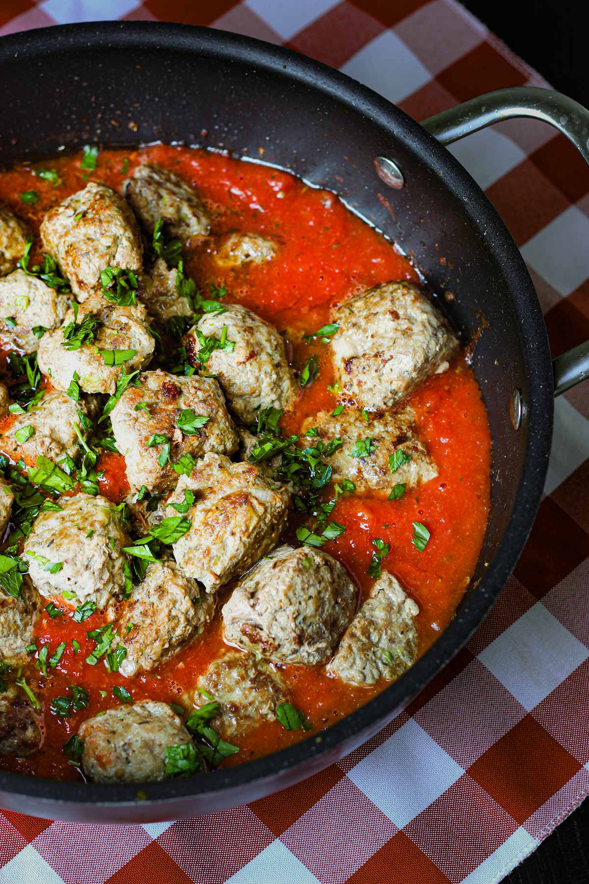 gluten-free meatballs in pot of red sauce on red checked cloth.