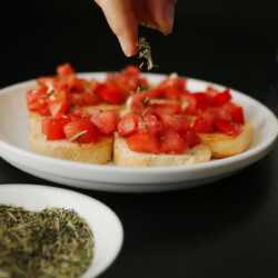 hand sprinkling herbes de provence on plate of bruschetta.