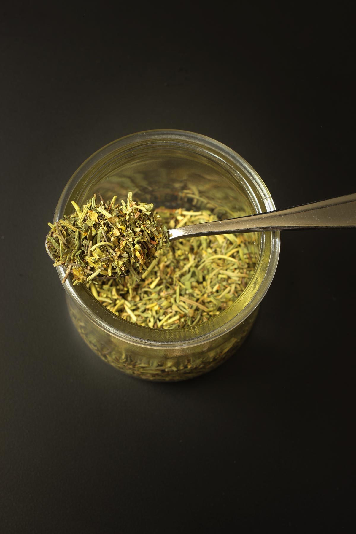 small spoon of herbes resting atop glass jar of more herbes.