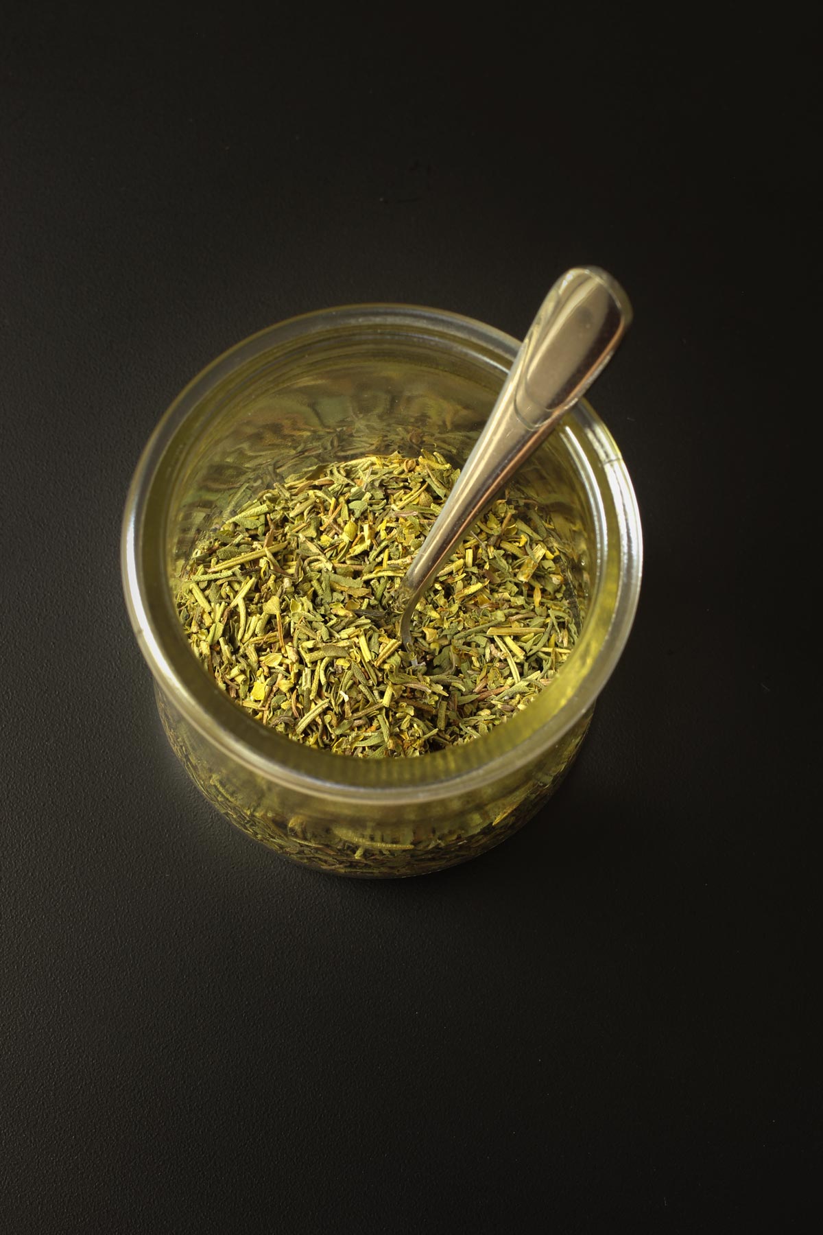 small spoon in glass dish of herbes for mixing the blend.