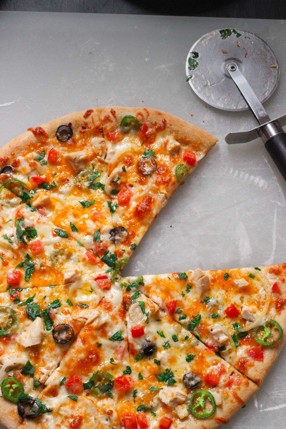 large jalapeño pizza with a piece missing on cutting board with pizza cutter