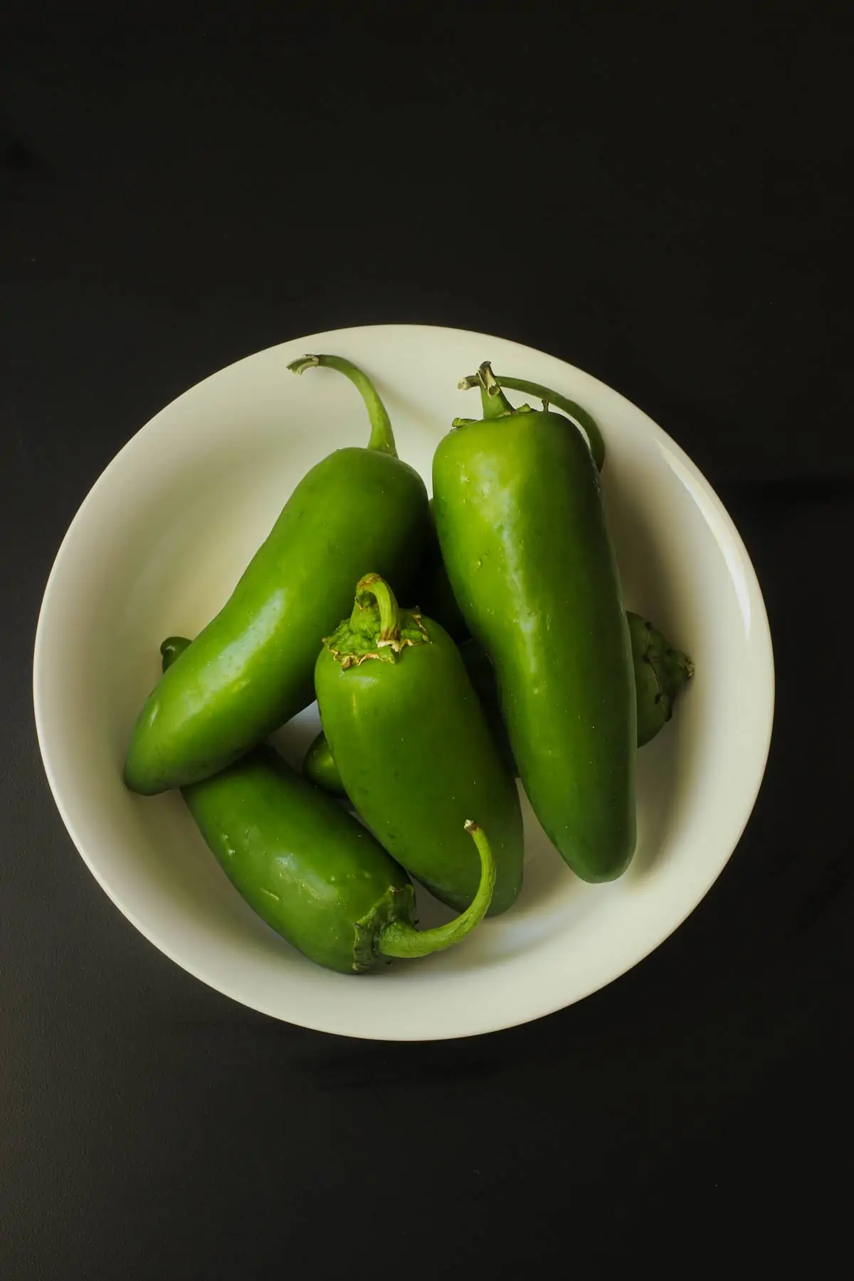 white bowl of jalapeños on black tabletop.