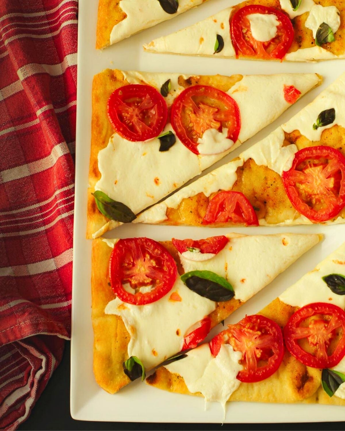 close up of margherita flatbread pizza with red printed cloth.