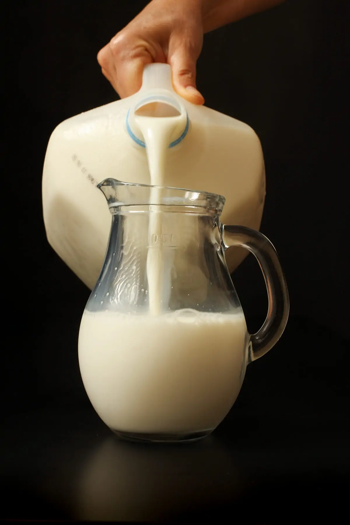 pouring milk out of plastic jug into smaller glass pitcher.