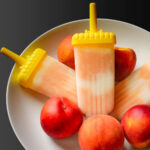 peach yogurt popsicles in their molds in a large white bowl of peaches.