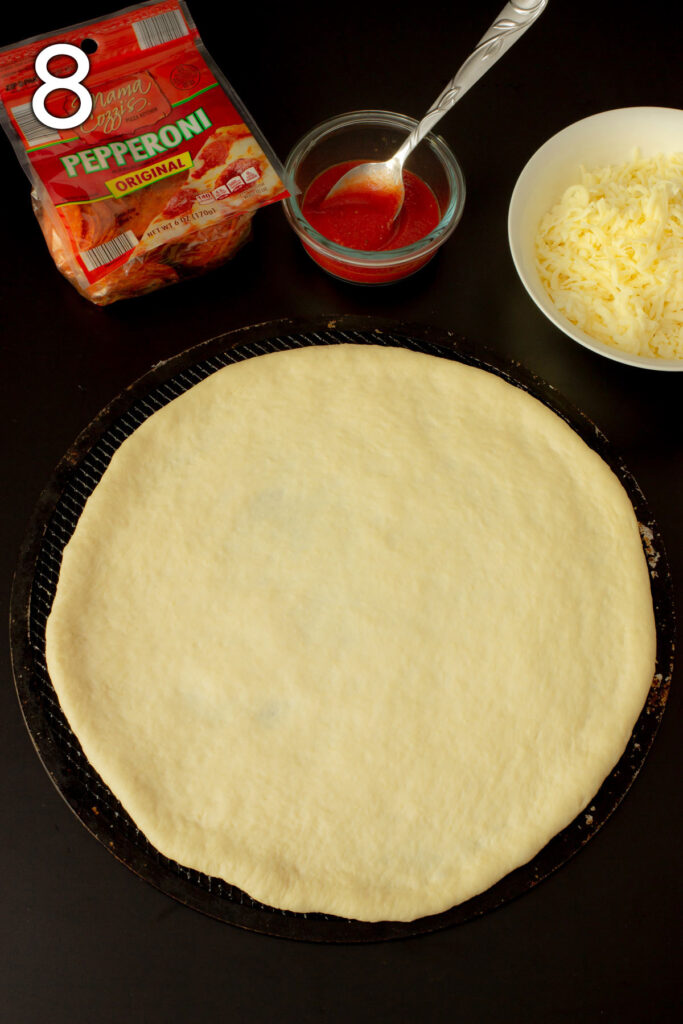 pizza dough shaped on a pizza screen next to different toppings.