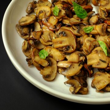 white plate of sauteed mushrooms sprinkled with basil leaves.