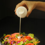 hand pouring buttermilk dressing onto salad.