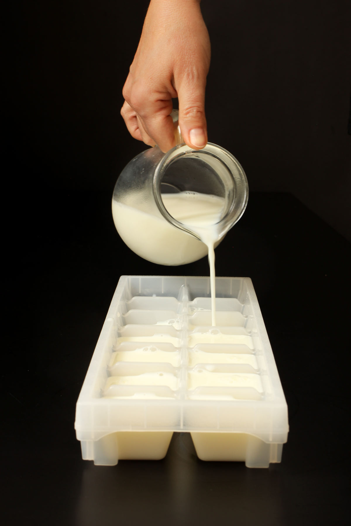 pouring milk into ice xube trays from small glass pitcher.