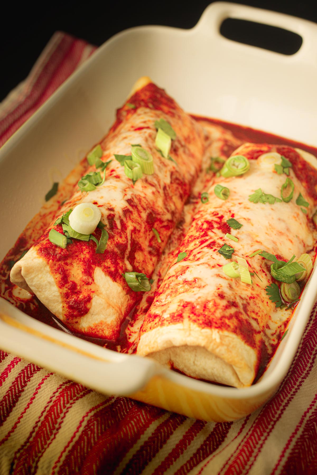 beef chimichangas in baking dish topped with sauce, cheese, and other toppings.