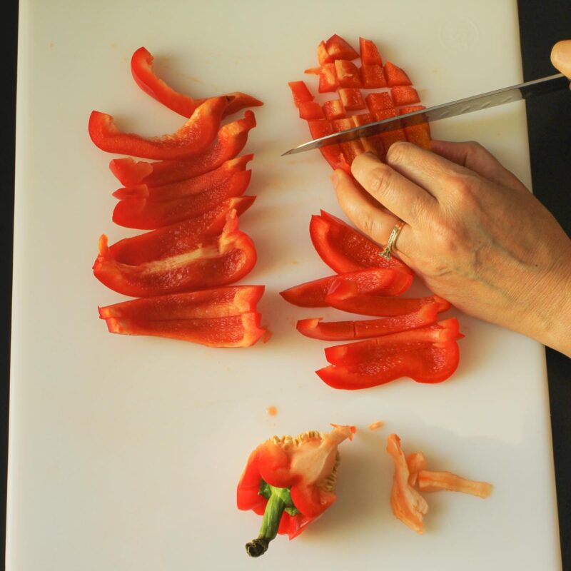 chopping and slicing red bell pepper on white cutting board.