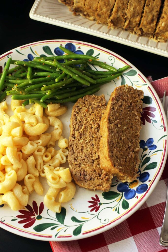 sliced meatloaf on dinner plate with green beans and macaroni and cheese.