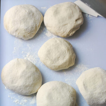 sourdough pizza dough balls on floured surface.