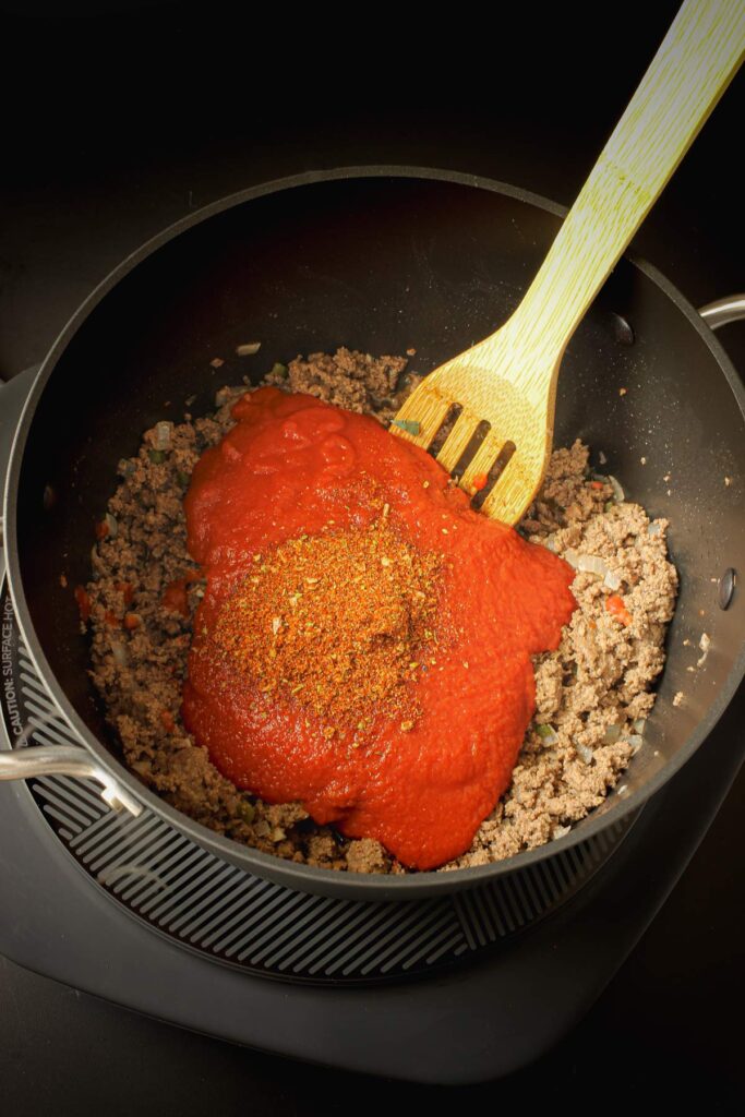 adding sauce and chili seasoning to ground meat in large pot.