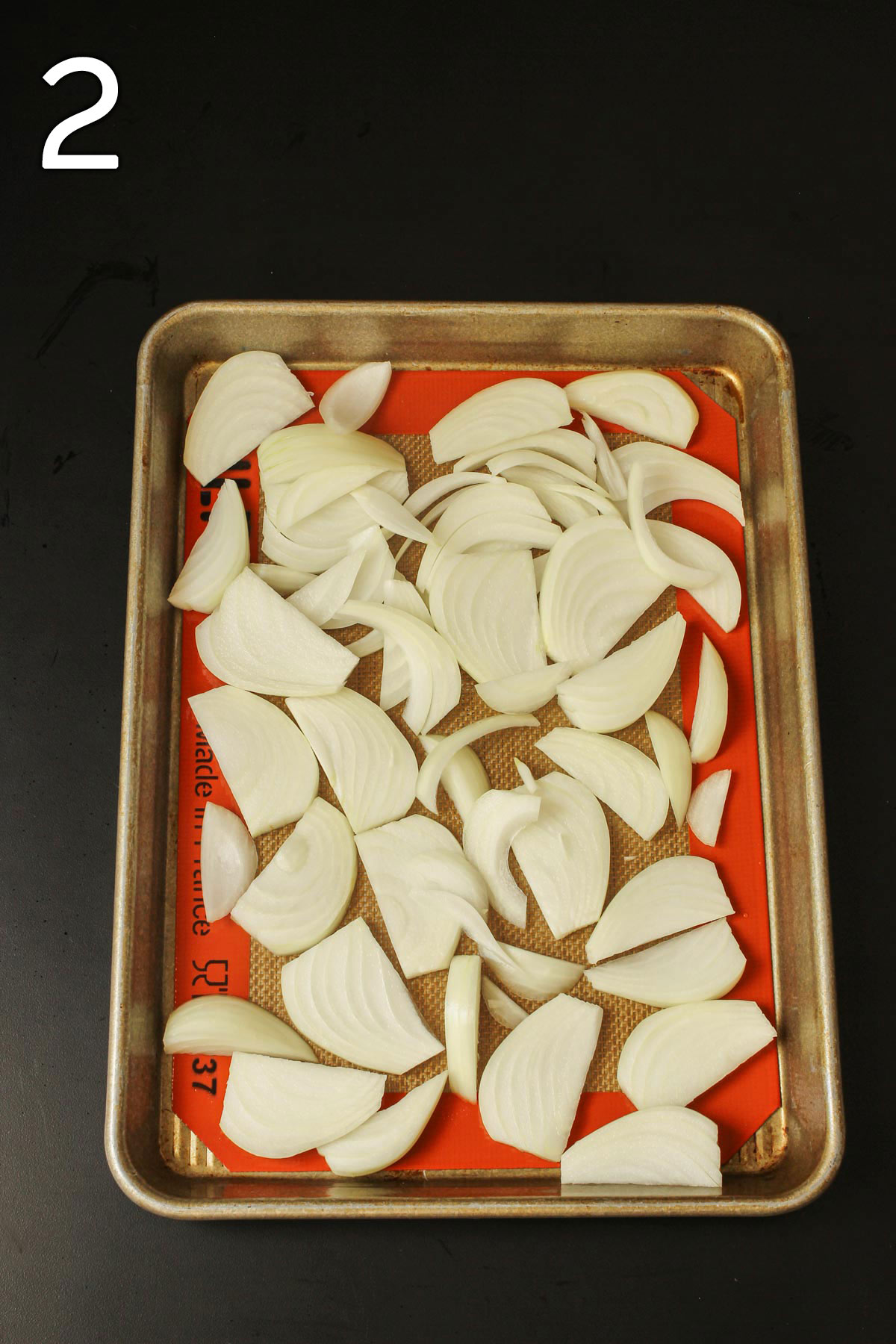 sliced onions spread on silpat mat on quarter sheet pan.